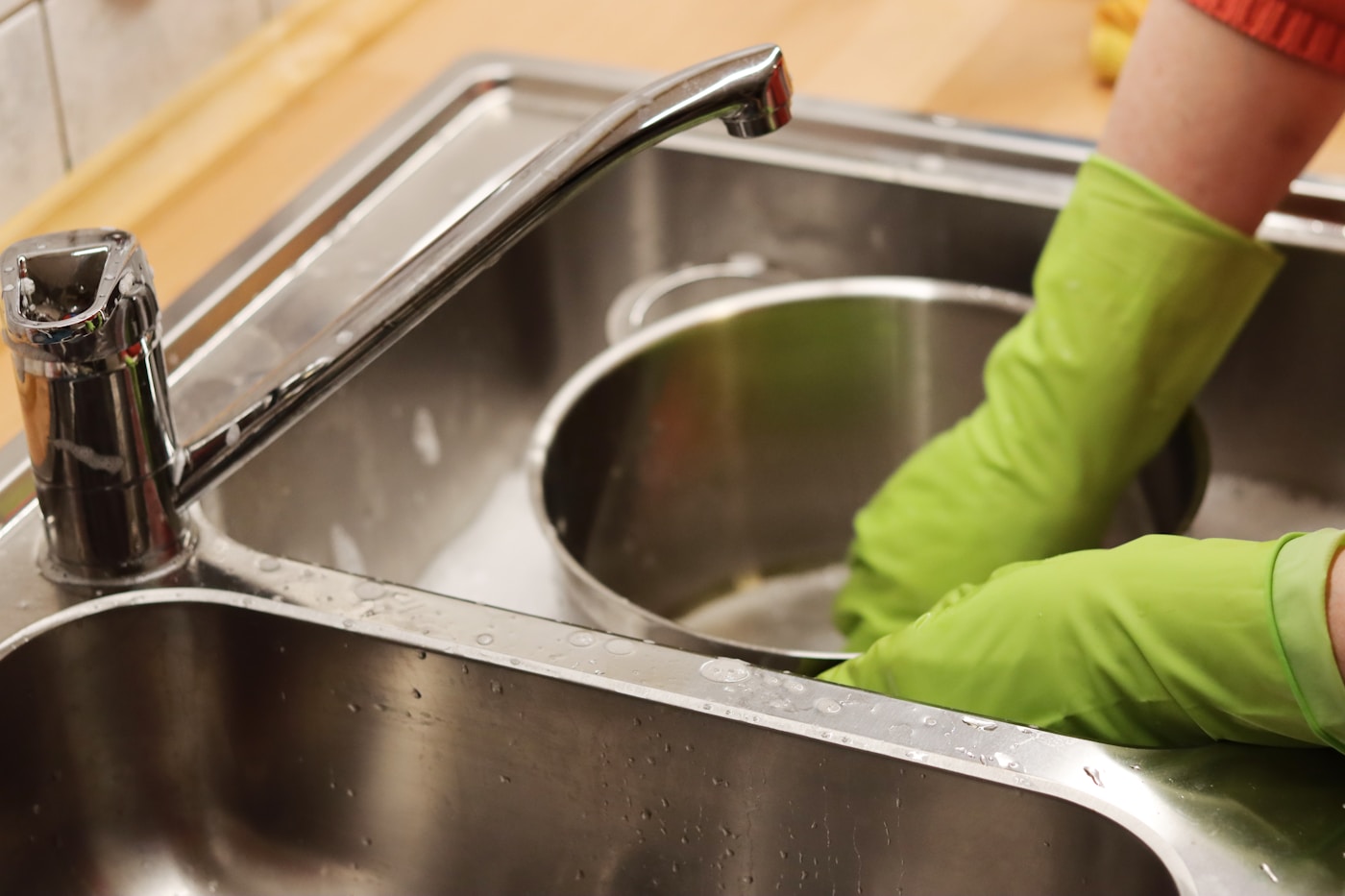 Gloved hand scrubbing a stainless steel kitchen sink
