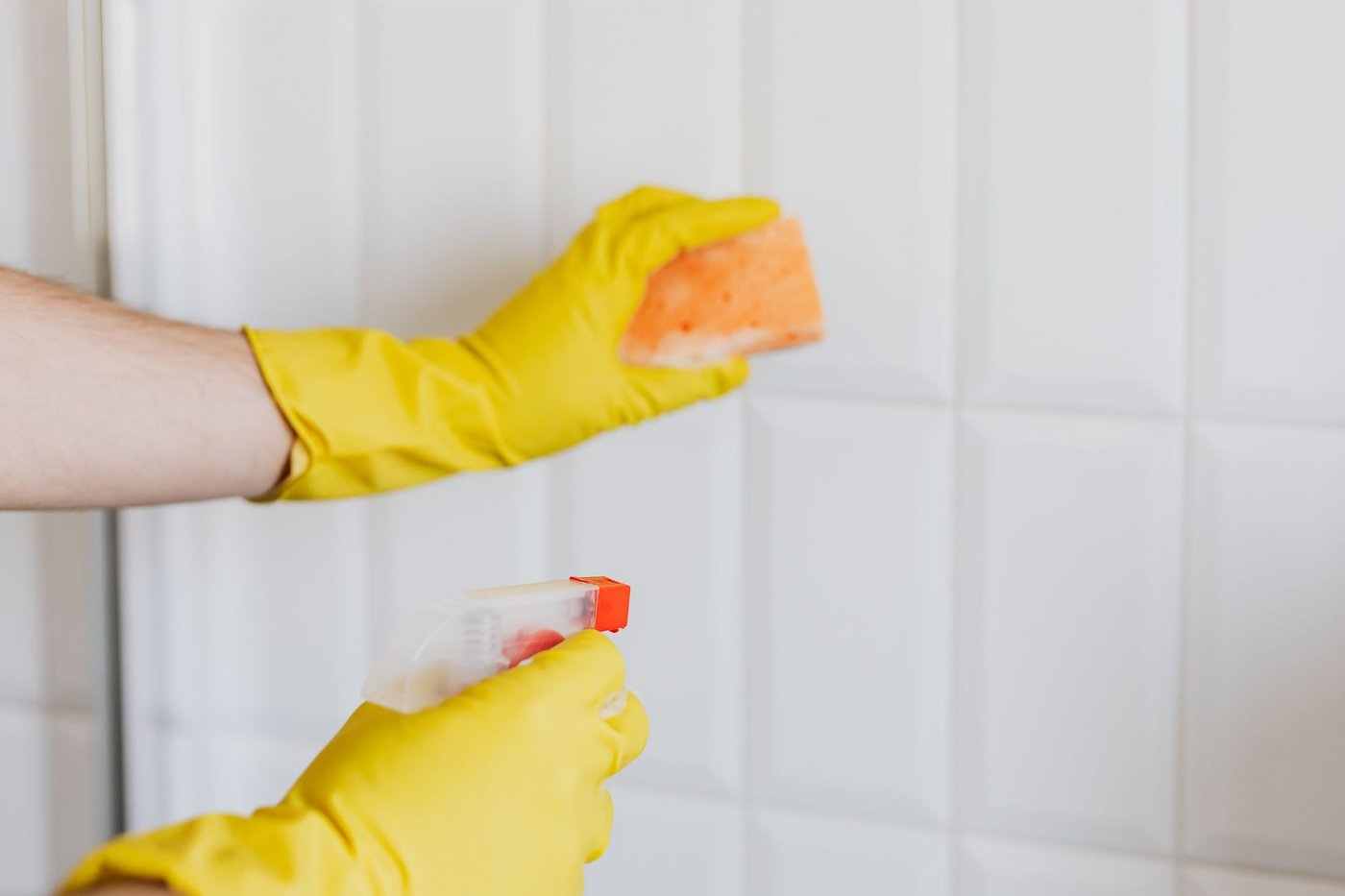 Gloved hands with a spray bottle and sponge cleaning white tile